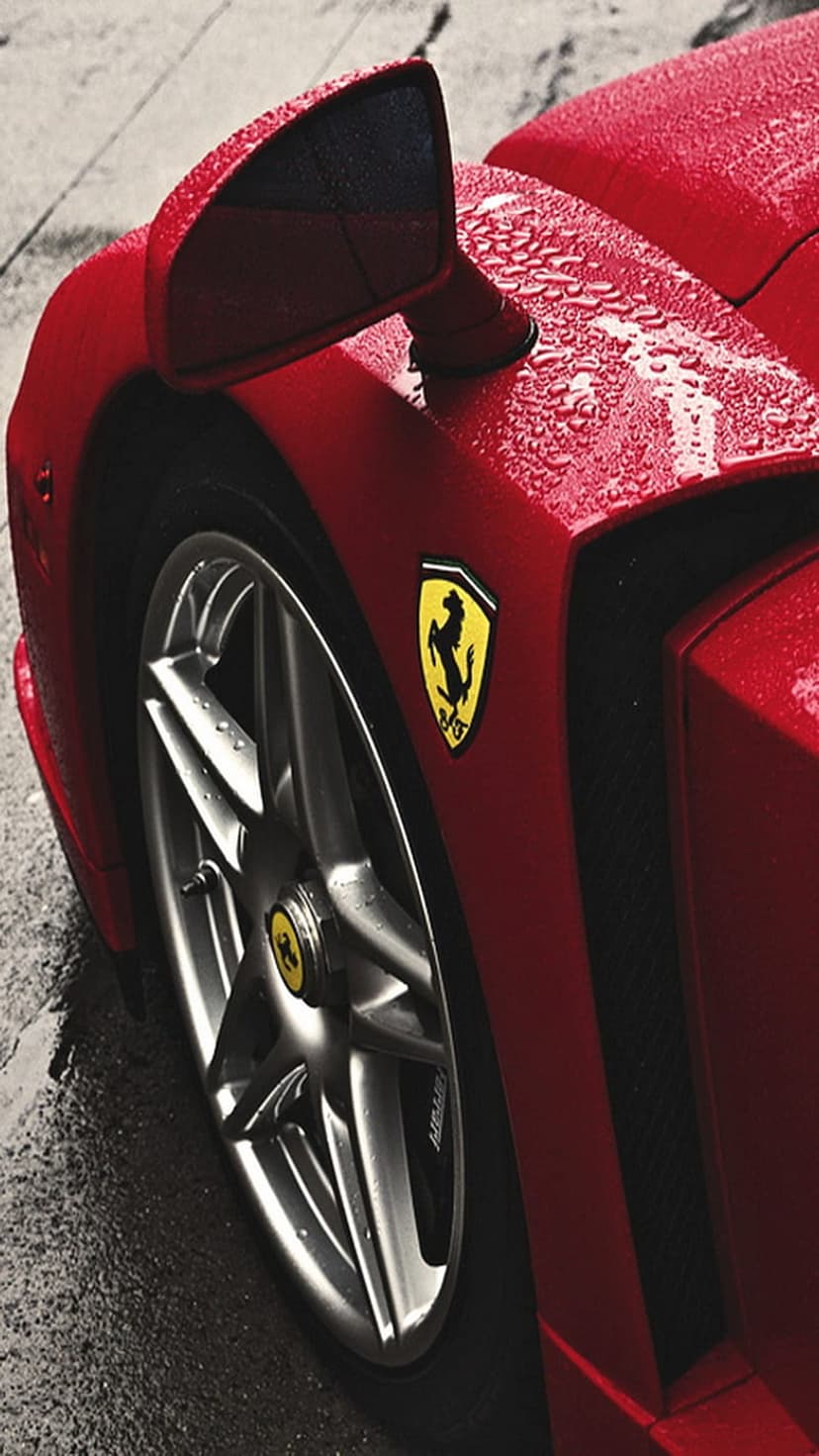 Red Ferrari fender with yellow prancing horse emblem and wet alloy wheel covered in glistening rain droplets.