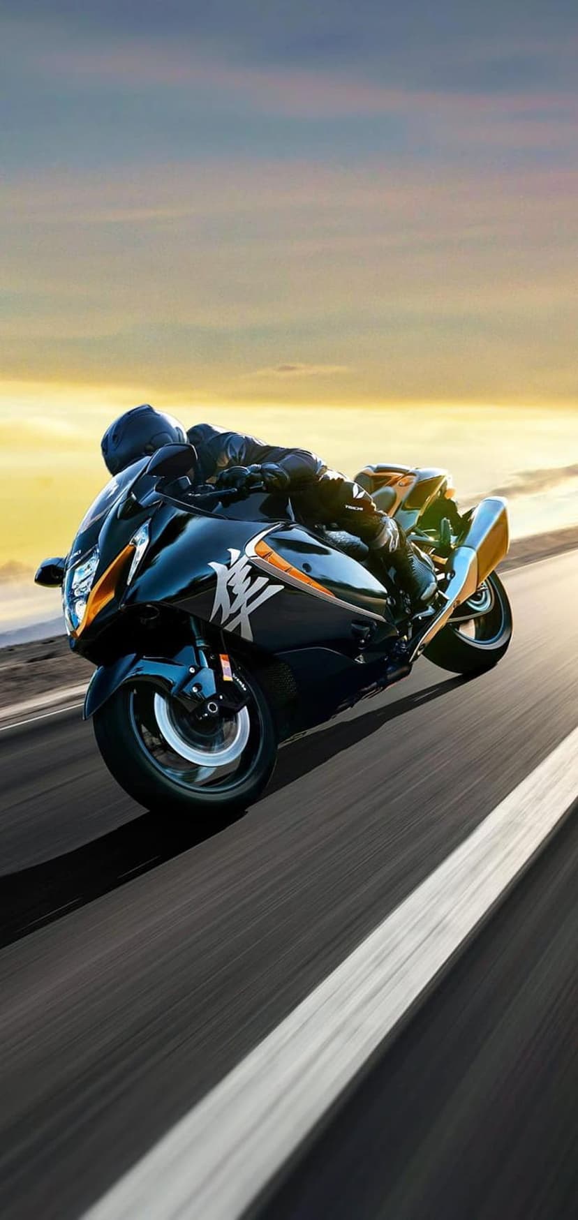 Black sport motorcycle with orange accents leans into a turn on an asphalt road during a vibrant sunset.