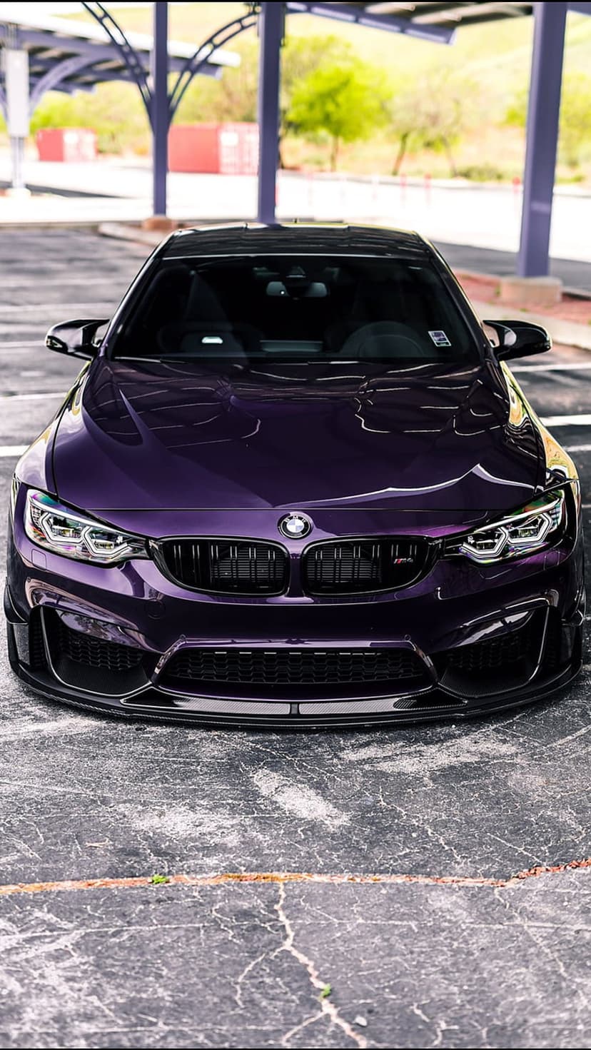 Purple BMW M4 Coupe with aggressive grilles parked under a modern canopy with purple pillars and urban greenery.