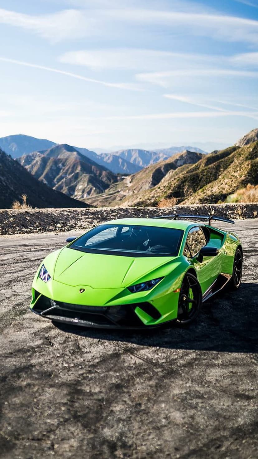Lime green Lamborghini Huracan parked on a dusty mountain road with rugged peaks and a clear blue sky background.
