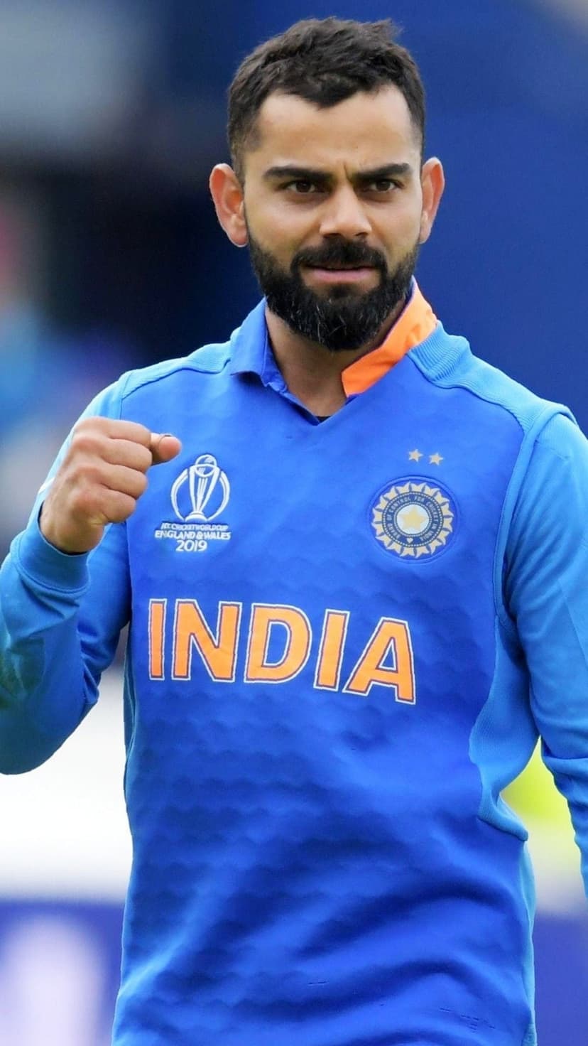 Virat Kohli clenches his fist in victory wearing a blue India cricket jersey with a fierce, focused expression.