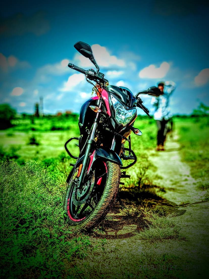 Sporty motorcycle parked on a green field with a blurred person walking away under a bright cloudy blue sky.