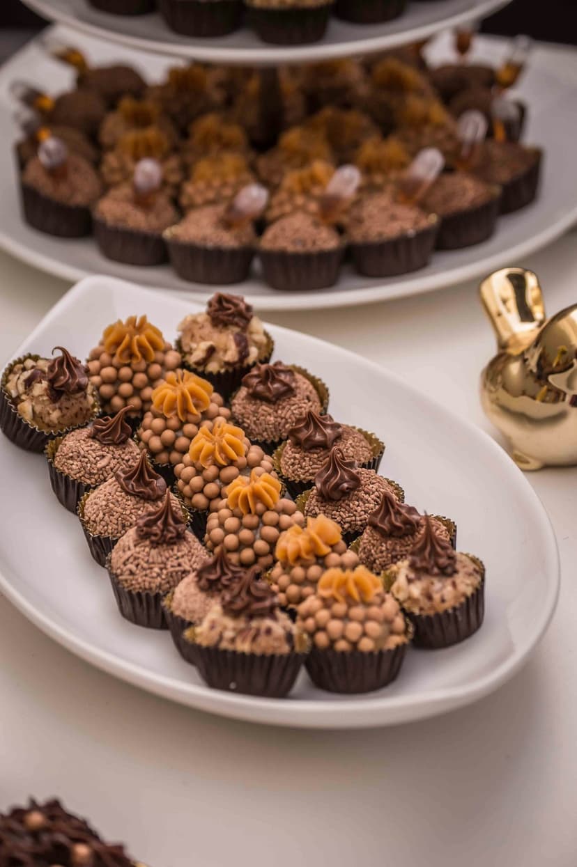 Gourmet chocolate brigadeiros with diverse toppings on a white platter next to a small golden bird figurine.