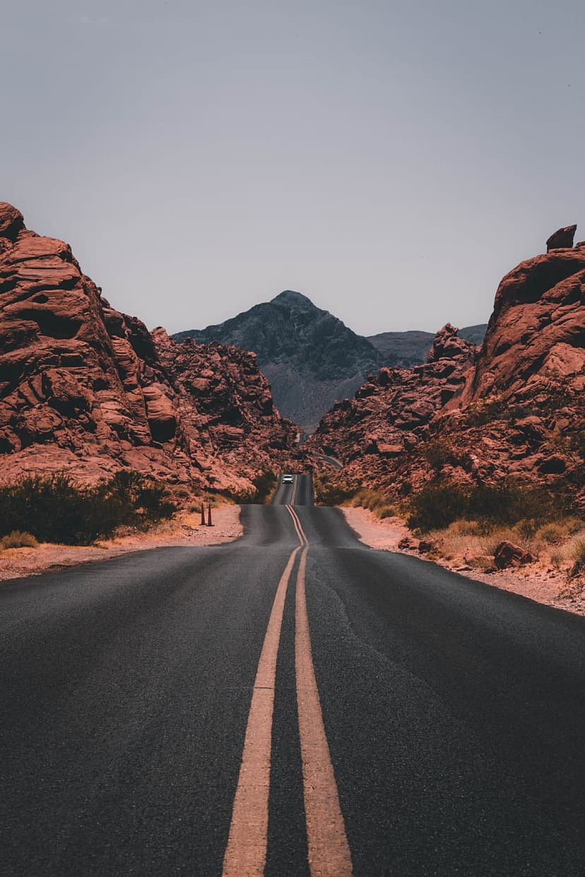 Winding asphalt highway with double yellow lines snakes through towering red sandstone formations and mesas.