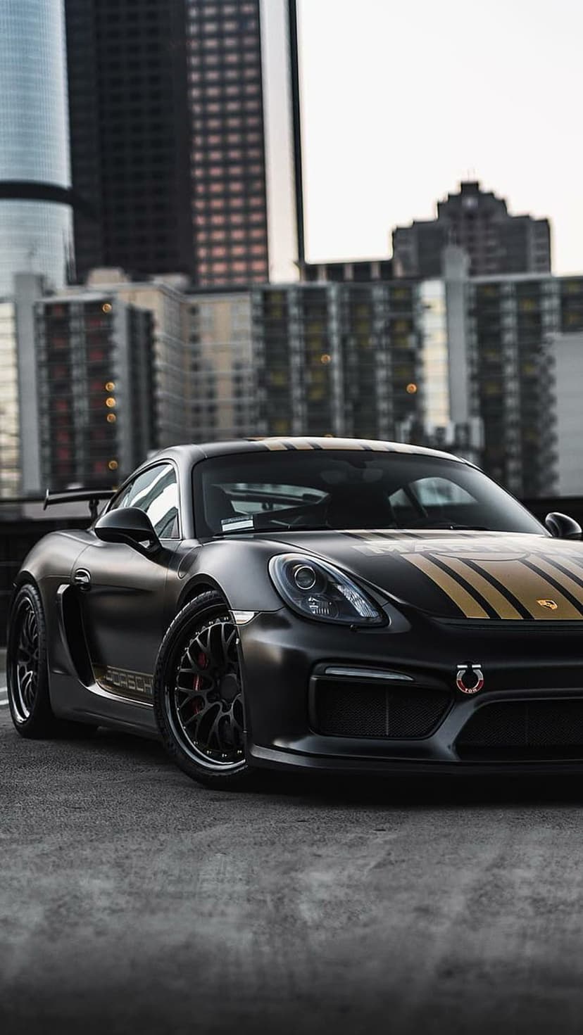 Porsche Cayman GT4 RS in matte black with gold stripes parked on a city street during a low-angle vertical shot.
