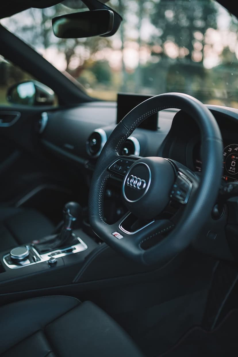 Audi leather steering wheel and center console with gear shift, dashboard vents, and rearview mirror visible.