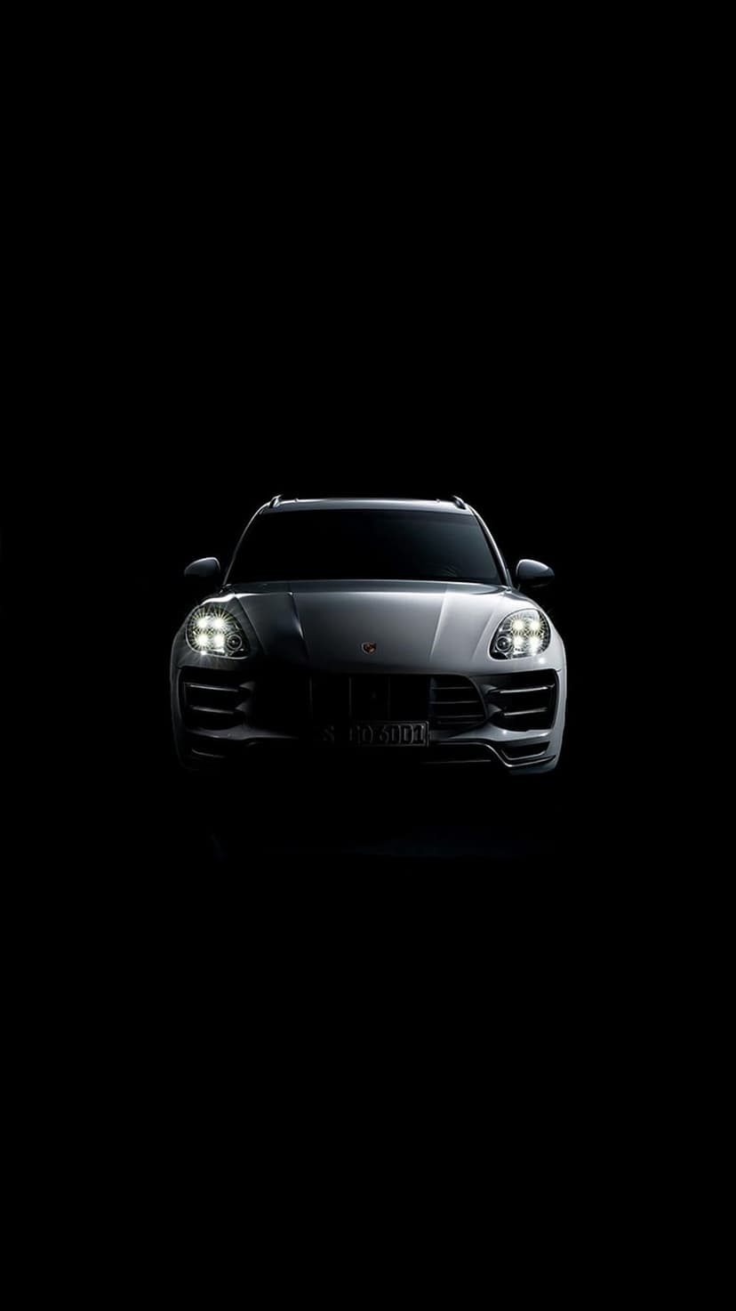 Porsche Macan SUV with glowing LED headlights and a sleek front grille isolated against a solid black background.