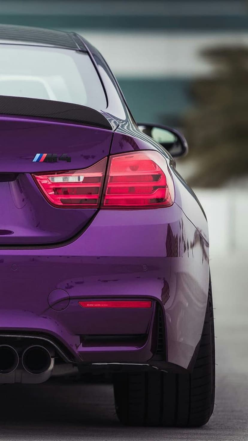 BMW M4 rear bumper with illuminated red tail lights, dual exhaust pipes, and purple metallic paint finish.