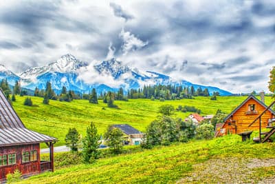 Lush Mountain Valley with Rustic Cabins and Snow-Capped Peaks
