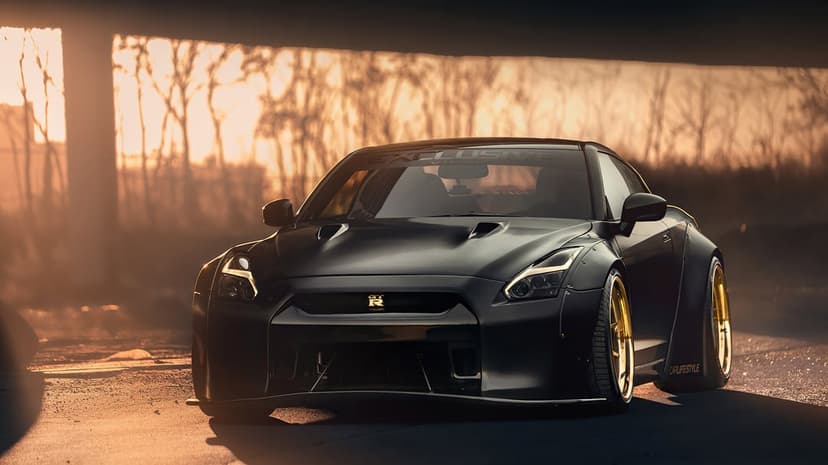Black Nissan GT-R widebody with gold wheels parked under a bridge during a warm golden hour sunset.
