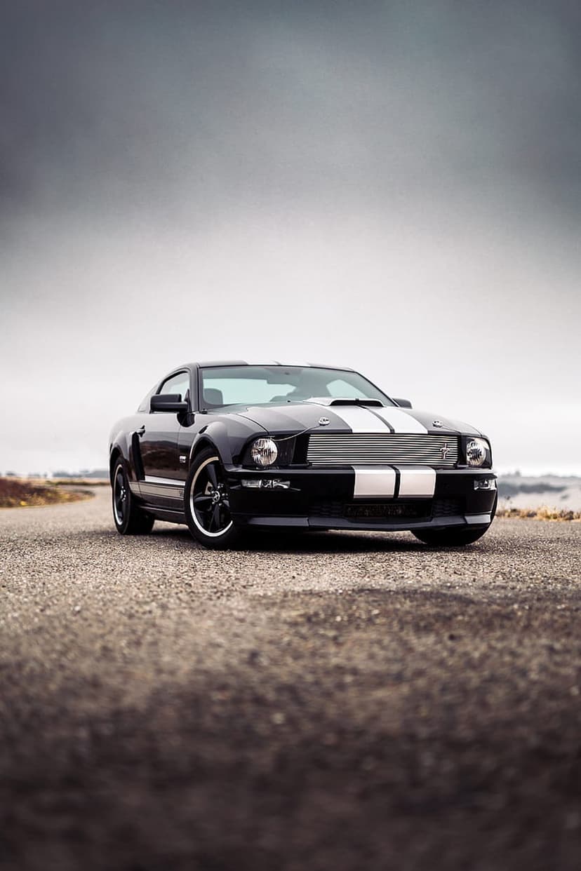 Ford Mustang GT with white racing stripes parked on textured asphalt featuring black rims and a moody sky.