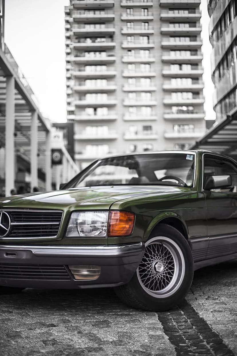 Vintage green Mercedes-Benz coupe parked on a cobblestone street with a modern skyscraper in the background.