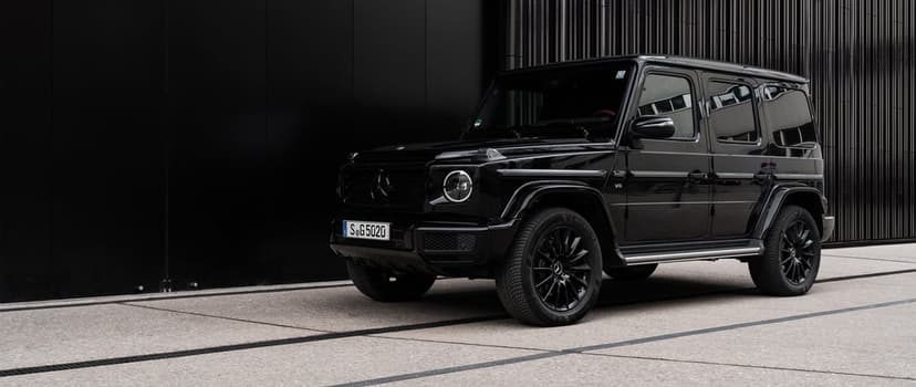 Black Mercedes-Benz G-Class SUV parked on concrete against a dark textured wall in an urban setting.