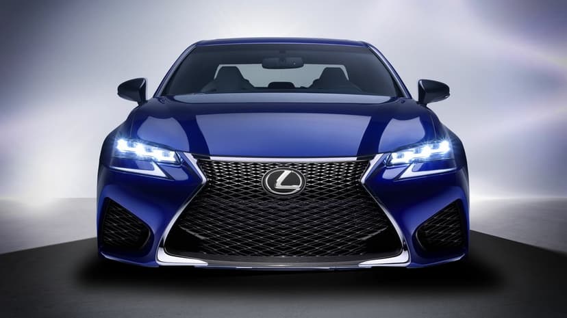 Front view of a blue Lexus sedan with glowing LED headlights and a large black mesh spindle grille.