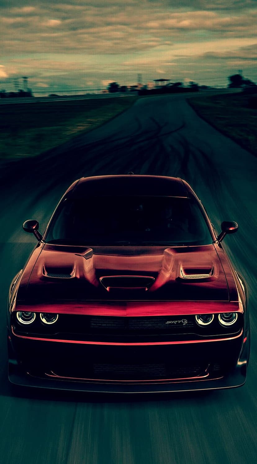 Red Dodge Challenger SRT Hellcat speeds on a race track under a cloudy sky with visible motion blur on wheels.