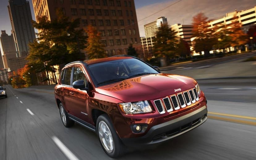 Red Jeep Compass SUV driving fast on a city street with autumn trees and skyscrapers during golden hour.