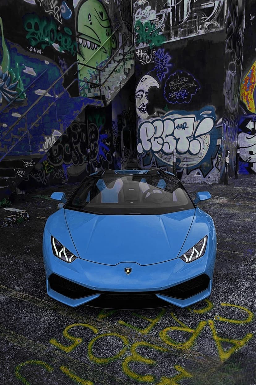 Blue Lamborghini convertible parked in a narrow alleyway surrounded by vibrant graffiti murals on brick walls.