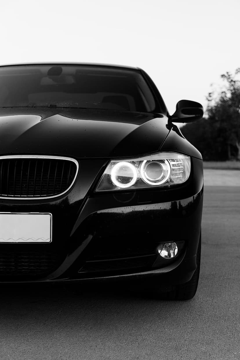 BMW sedan front grille and circular glowing headlights in a high-contrast black and white close-up shot.