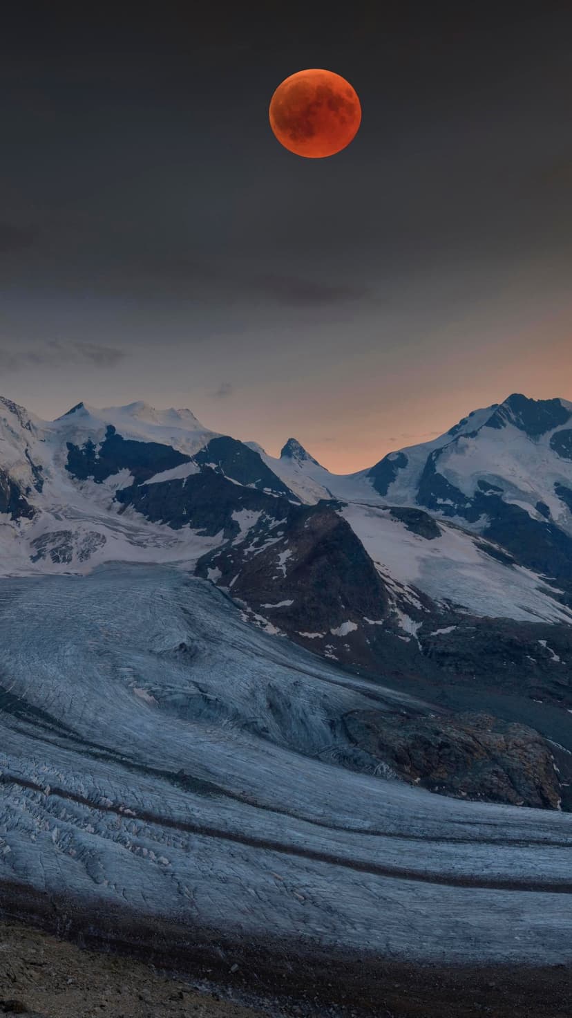 Crimson moon glowing in a purple twilight sky above jagged snow-covered mountain ridges and a textured glacier.
