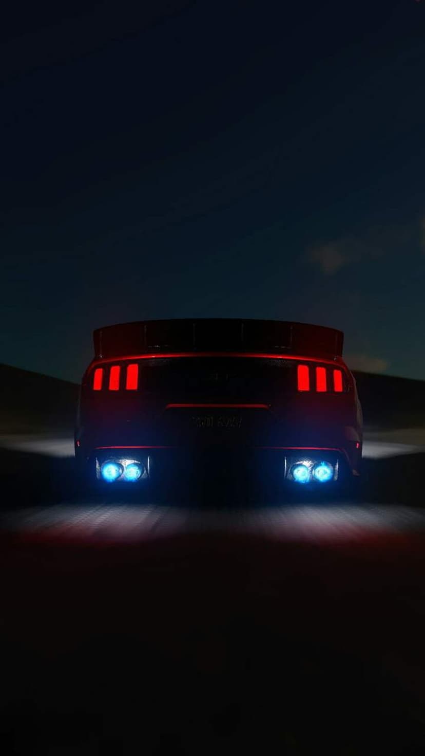 Red Ford Mustang rear view with glowing red taillights and blue exhaust flames against a dark night sky.