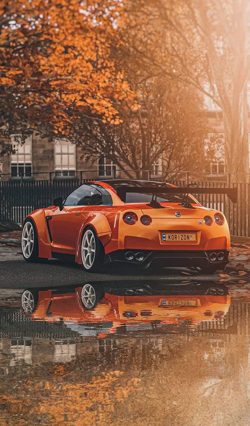 Nissan GT-R in metallic orange reflects on a wet road surrounded by fallen autumn leaves during a golden sunset.