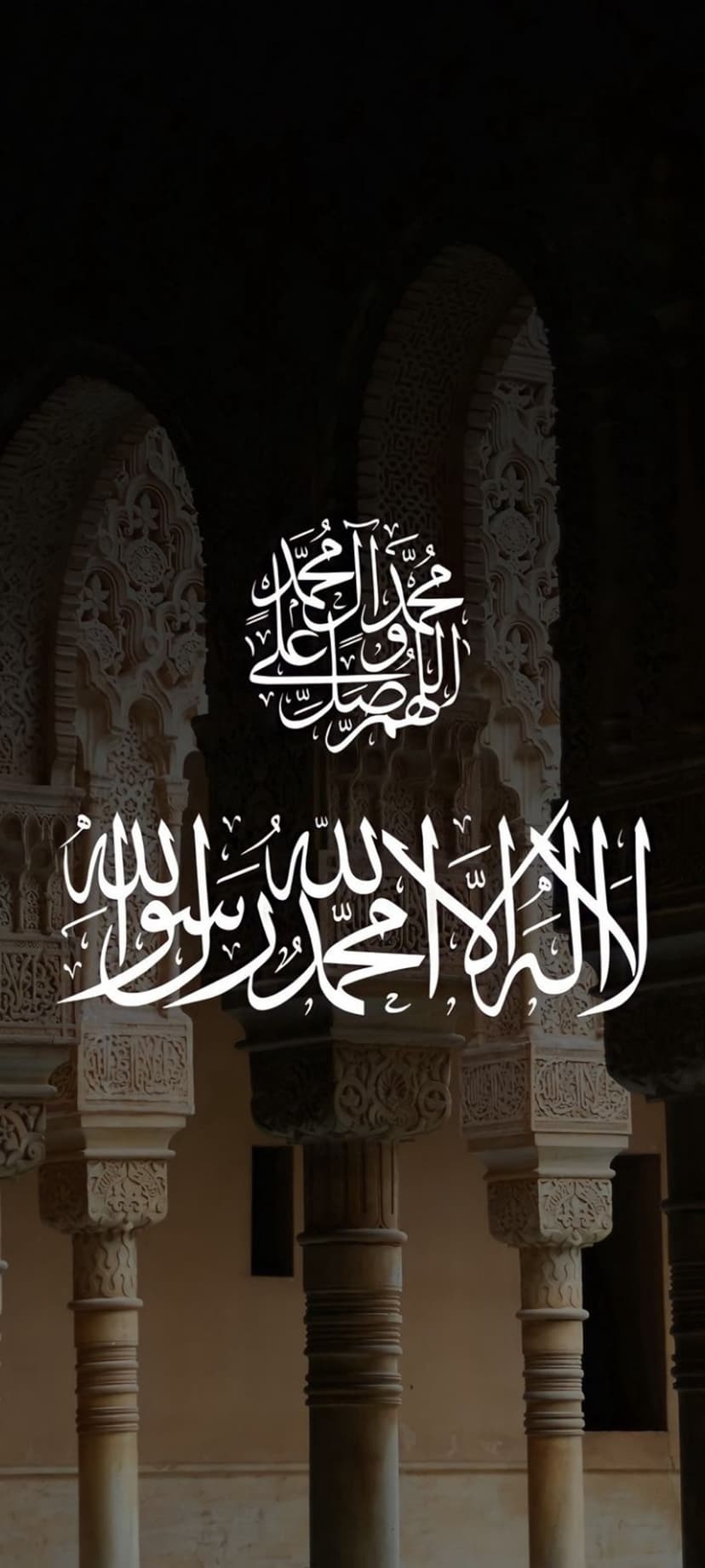 White Arabic calligraphy carved into a dark stone archway within the Alhambra palace in Granada, Spain.