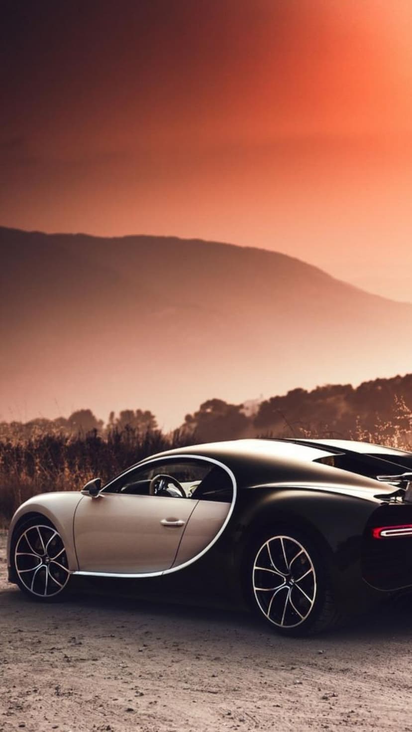 Bugatti Chiron hypercar parked on a dirt path against a glowing orange sunset sky and hazy mountain silhouettes.