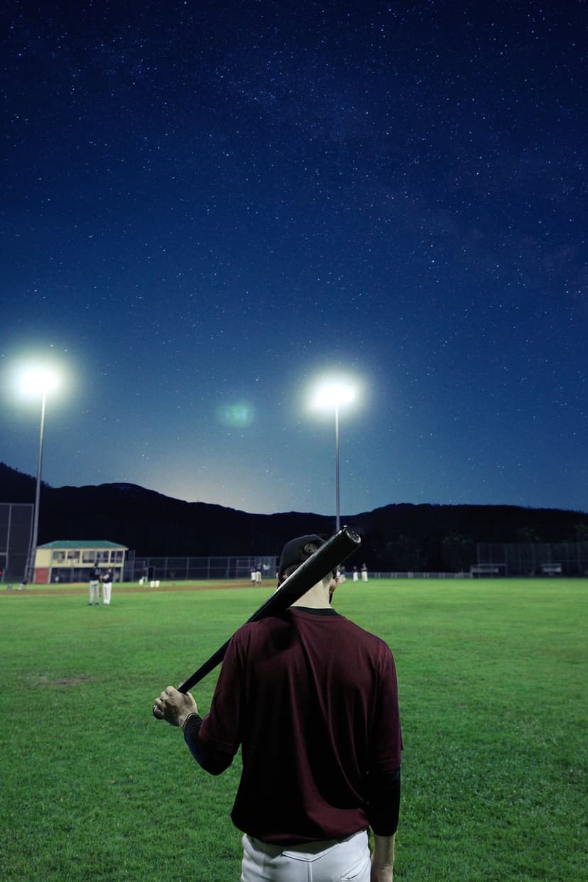 Baseball player with a bat over his shoulder stands on a field beneath a starry sky and distant mountain peaks.