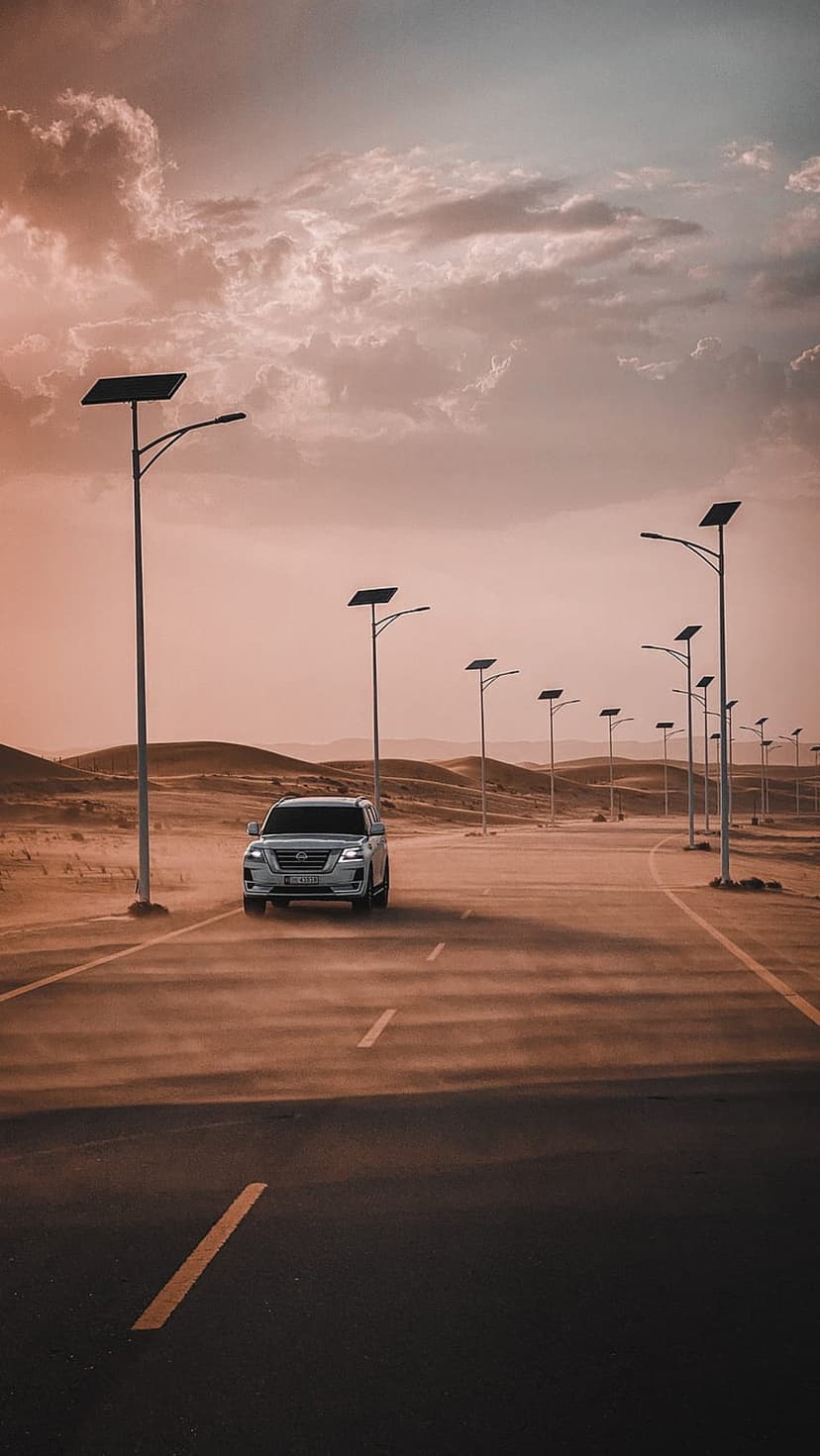 White SUV driving on a desert highway lined with solar streetlights under a dramatic orange and purple sky.