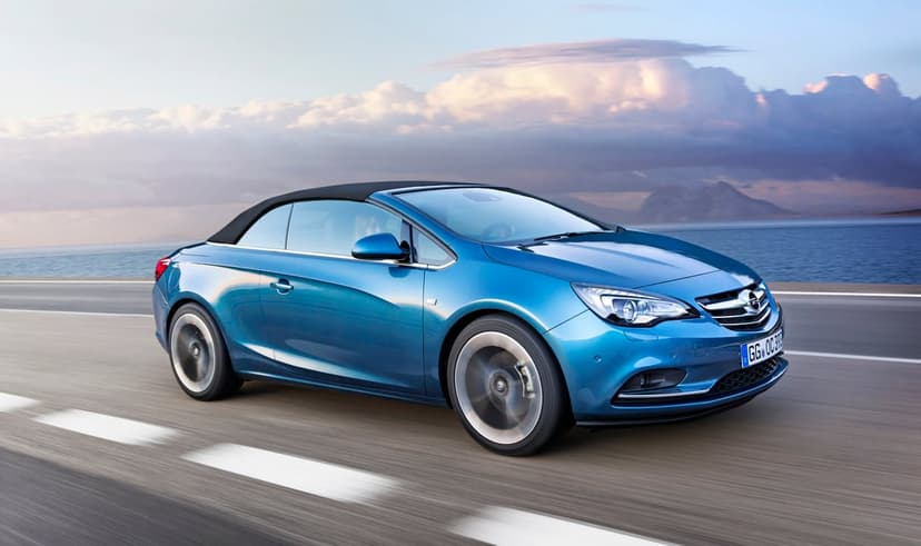 Blue convertible car driving on a coastal road at sunset with motion blur and a cloudy sky.