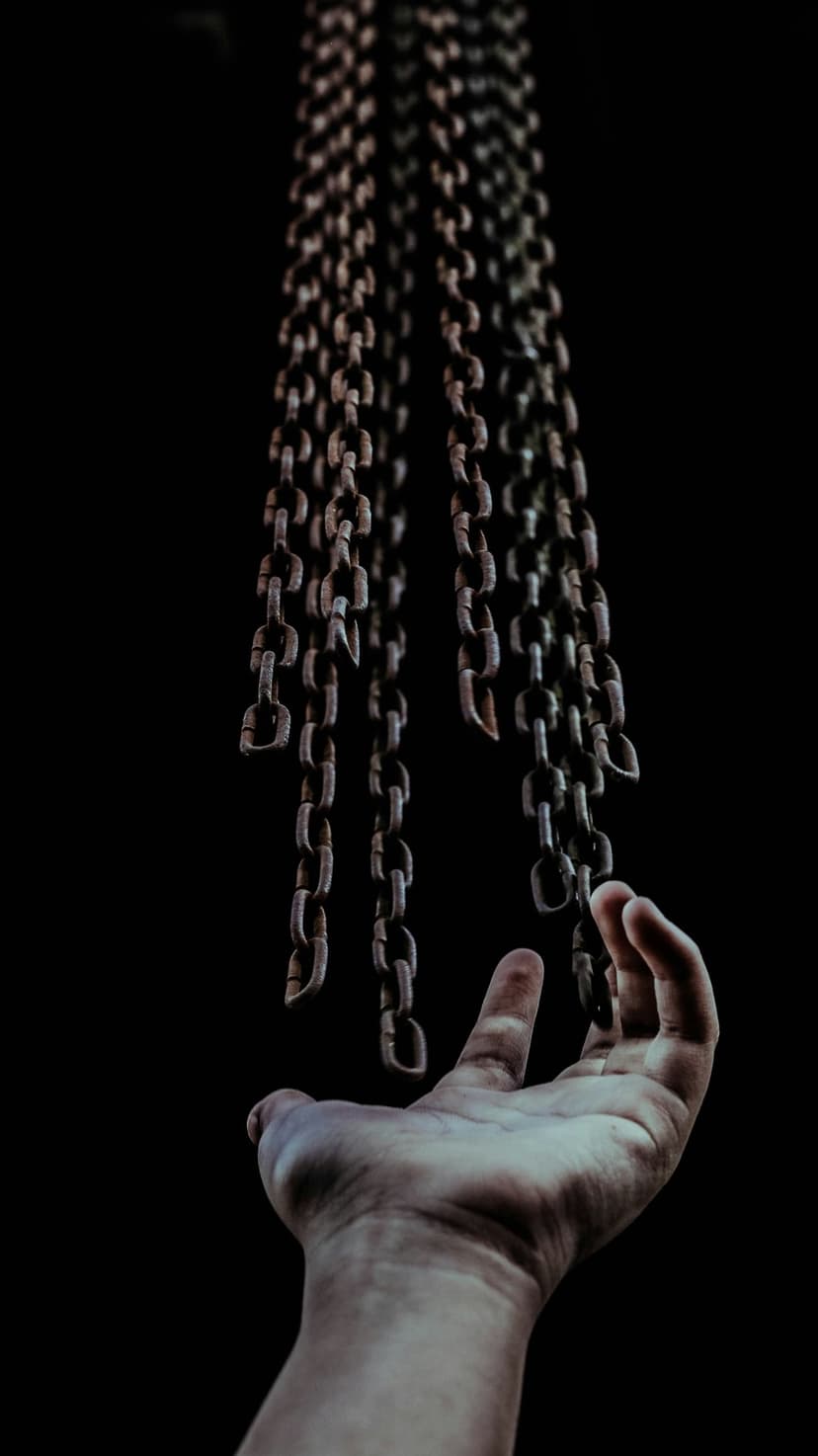 Rusty iron chains hang vertically over a person's open palm against a solid black background with sharp lighting.