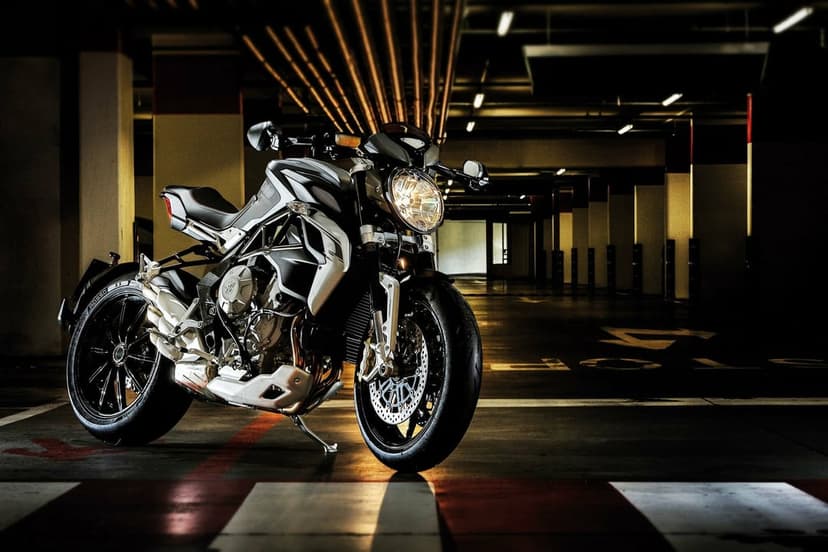 Silver naked motorcycle parked in a dark underground garage with dramatic lighting and industrial pipes.