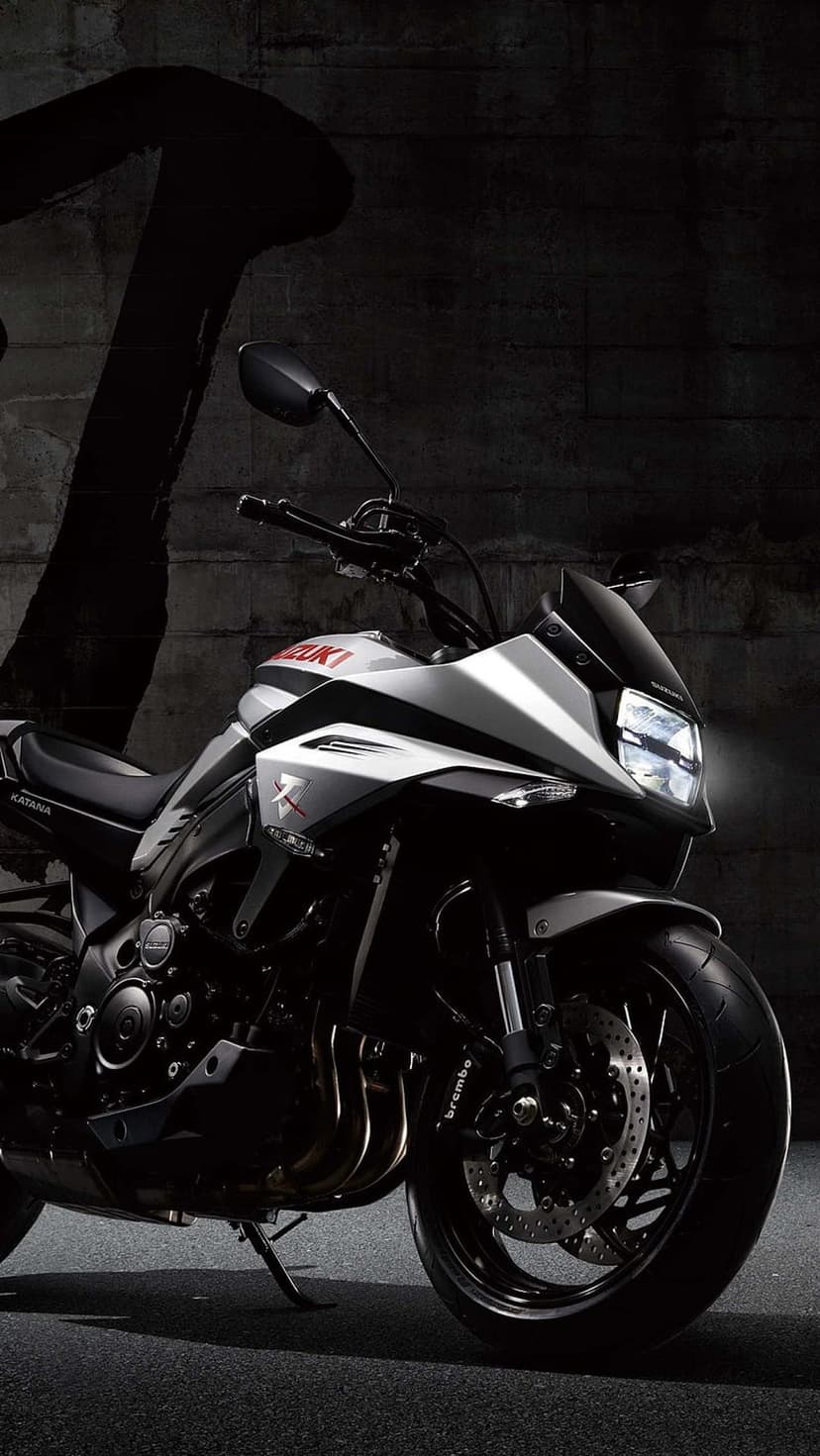 Suzuki Katana motorcycle with silver bodywork parked against a textured gray concrete wall in low light.