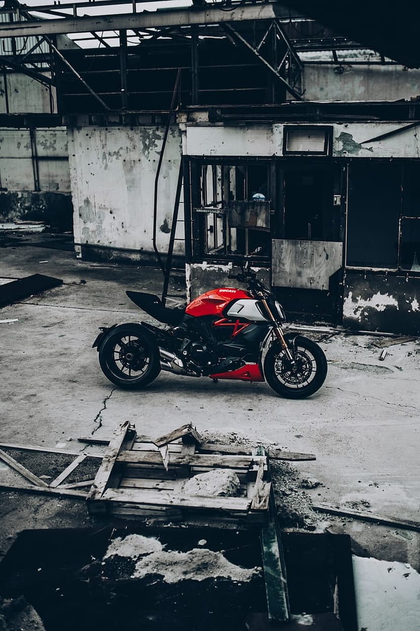 Red Ducati motorcycle parked on cracked concrete inside a derelict warehouse with peeling walls and debris.