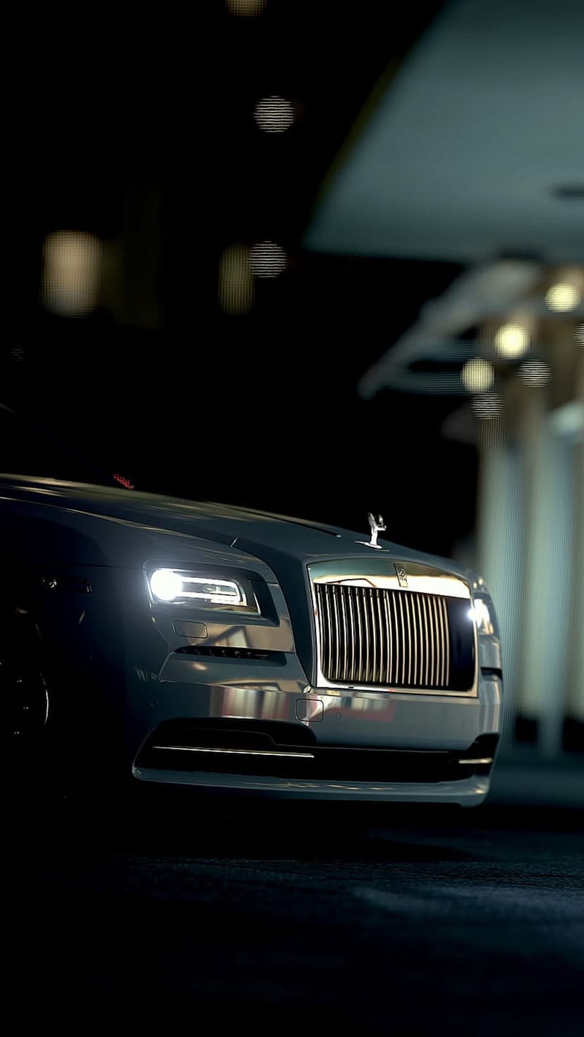 Rolls-Royce Wraith front end with glowing headlights and Spirit of Ecstasy ornament during a dark urban night.