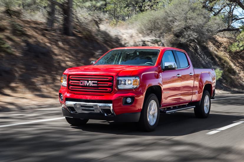 Red GMC Canyon pickup truck driving on a winding mountain road with motion blur and a sunny forest background.