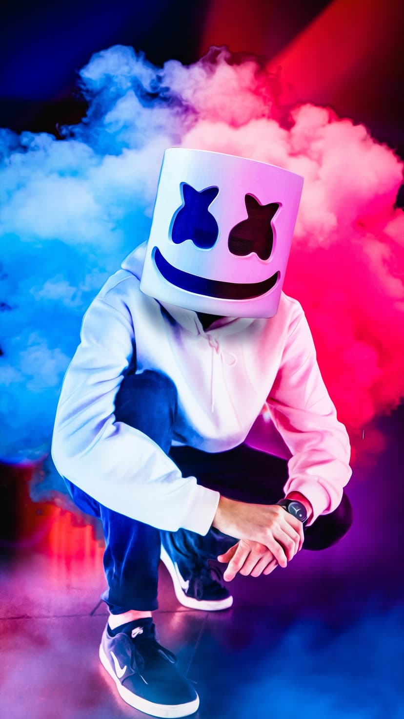 DJ Marshmello wearing a white bucket mask and hoodie, crouching within thick blue and pink neon smoke clouds.