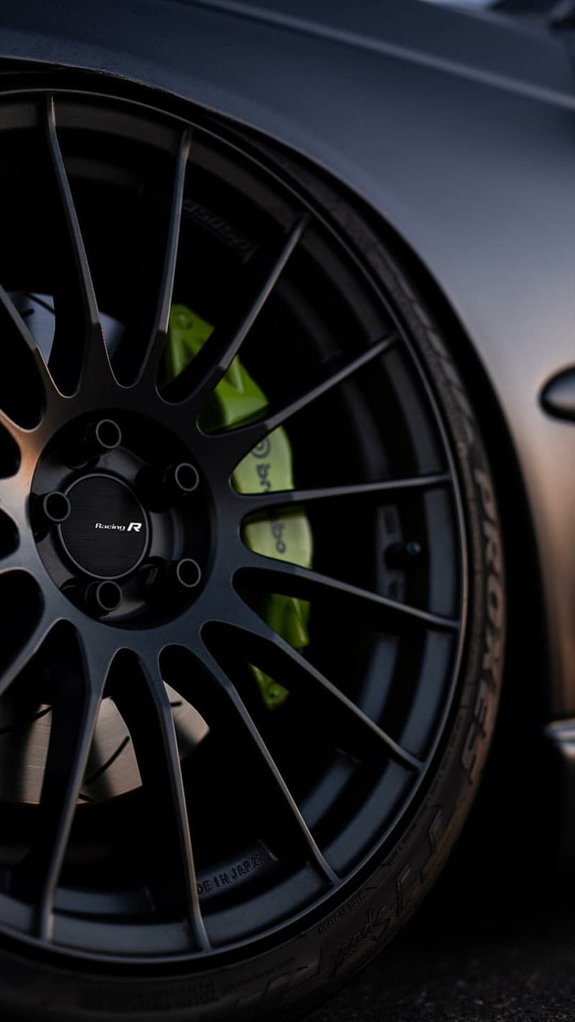 Black multi-spoke car rim with a neon green brake caliper and branded tire sidewall in a low-angle shot.