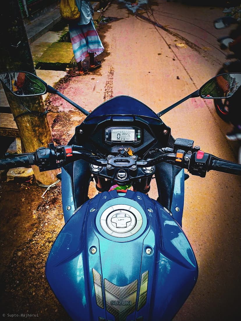 Blue Suzuki motorcycle handlebars and digital speedometer display seen from a rider's perspective on a sunny day.
