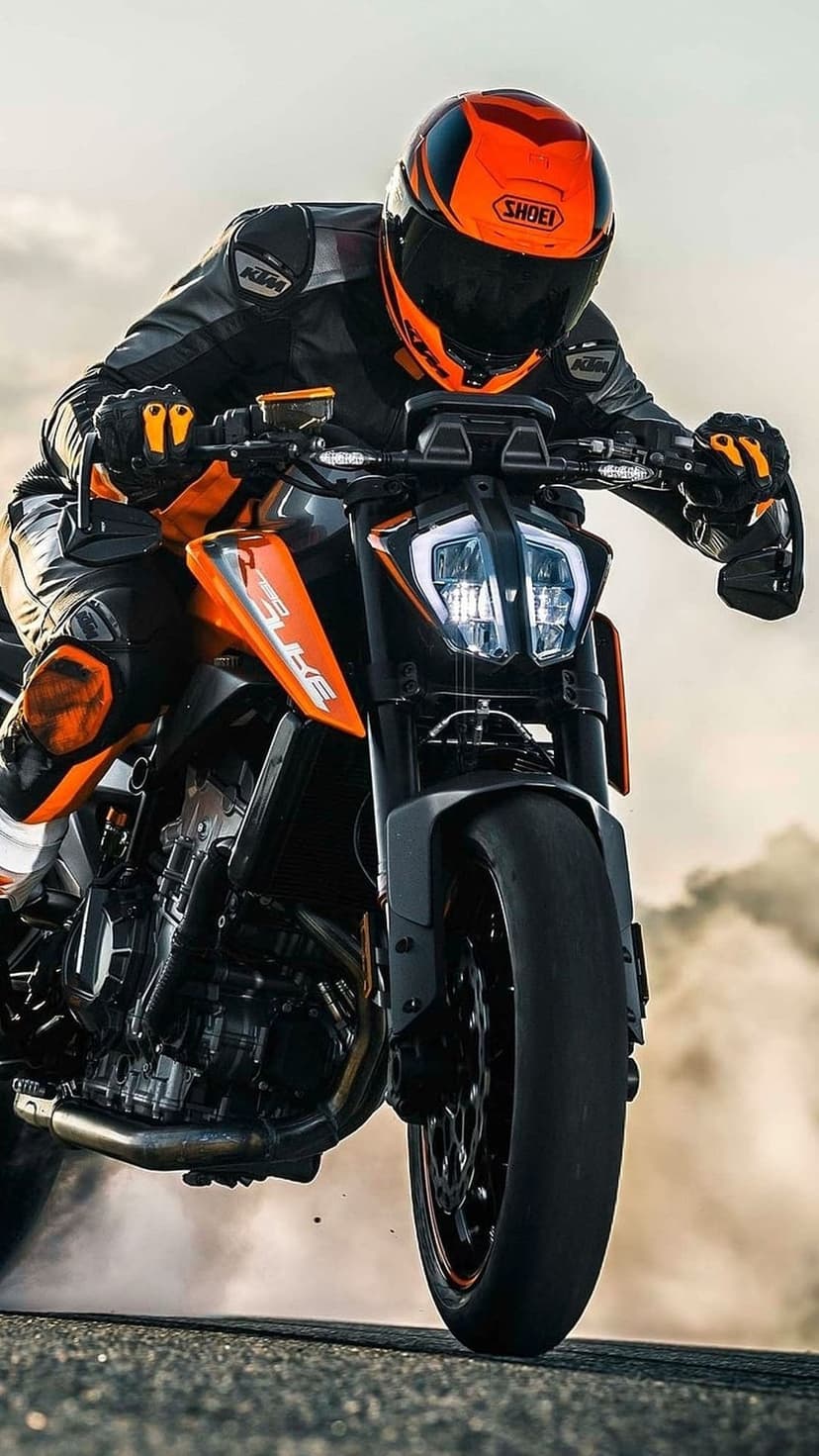 Motorcyclist in an orange helmet leans a KTM bike through smoke, creating a dynamic vertical racing scene.