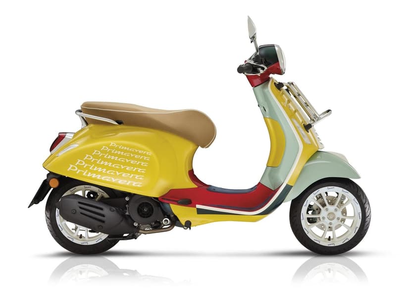 Side view of a yellow and mint green Vespa scooter with a tan seat against a white background with reflection.