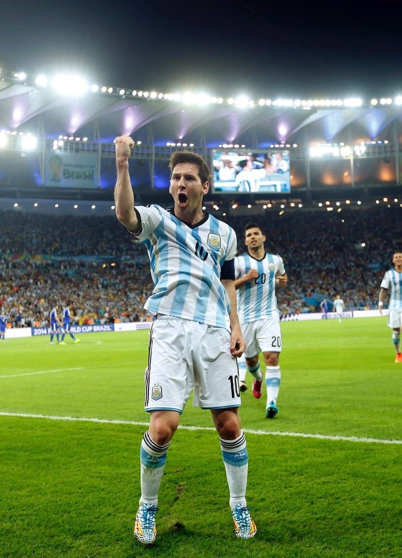 Lionel Messi raises a fist while celebrating a goal in his blue and white Argentina jersey on a green pitch.