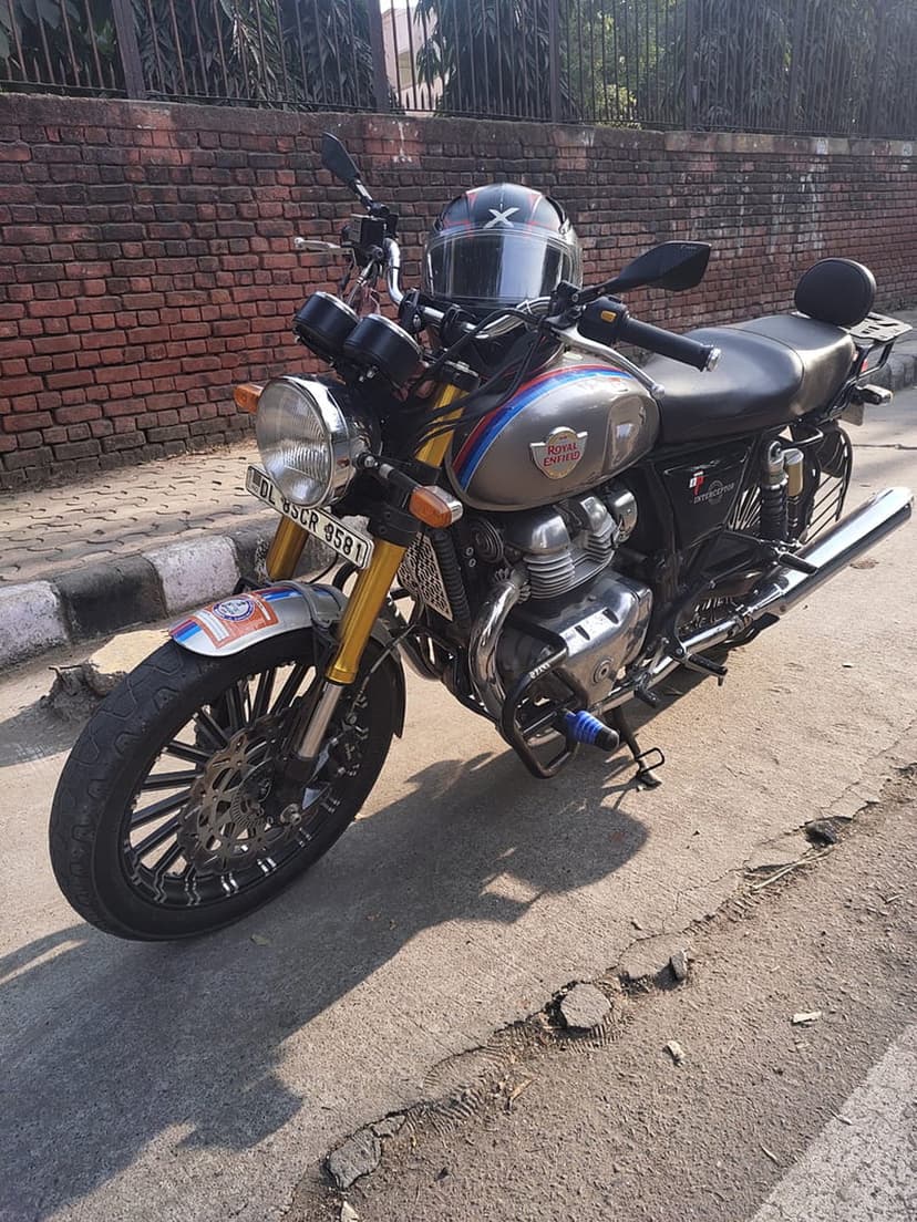 Royal Enfield Interceptor 650 motorcycle with red stripes and a black helmet parked against a brick wall.