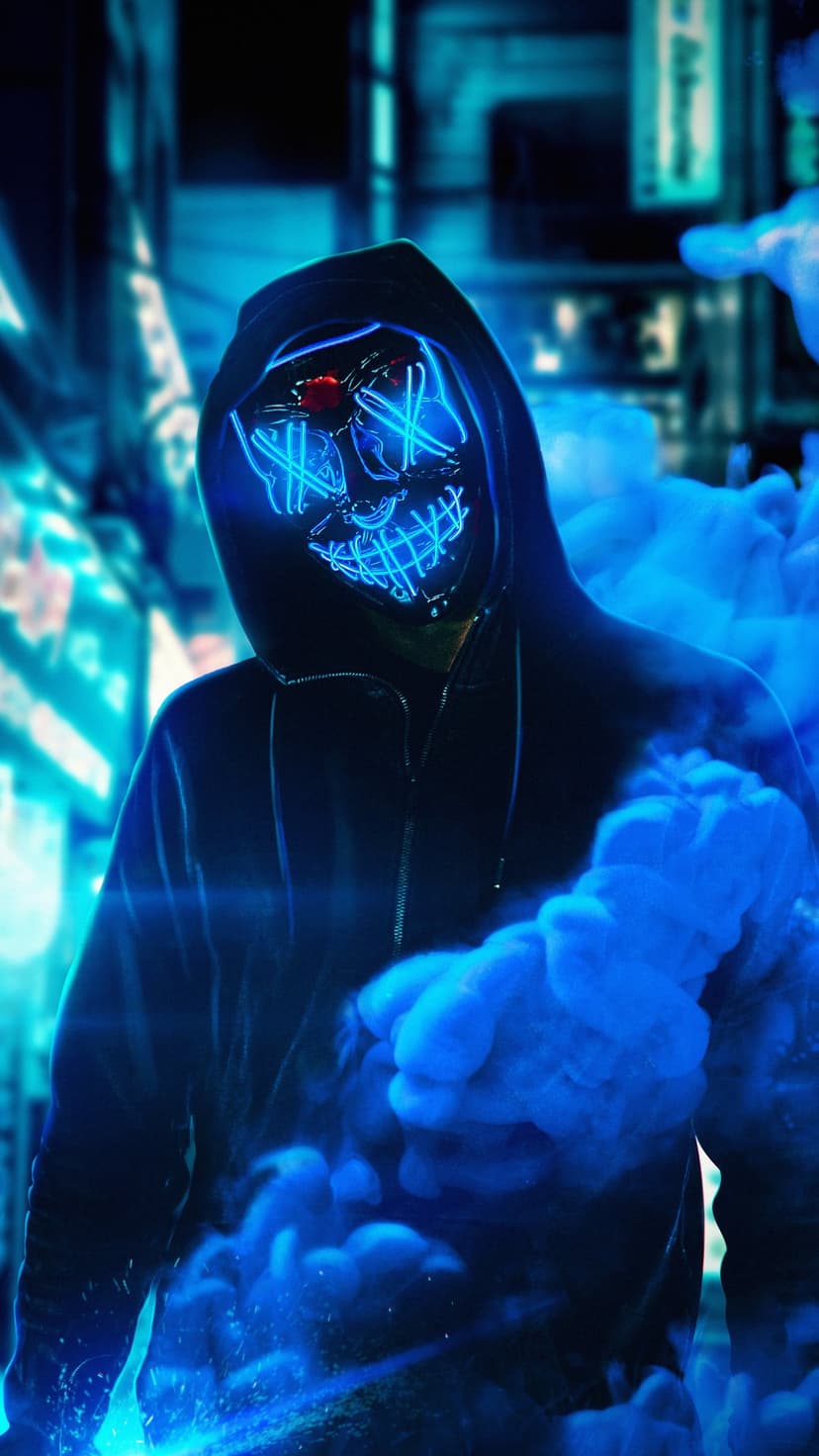 Person wearing a glowing blue LED mask surrounded by thick smoke against a blurred nighttime city background.