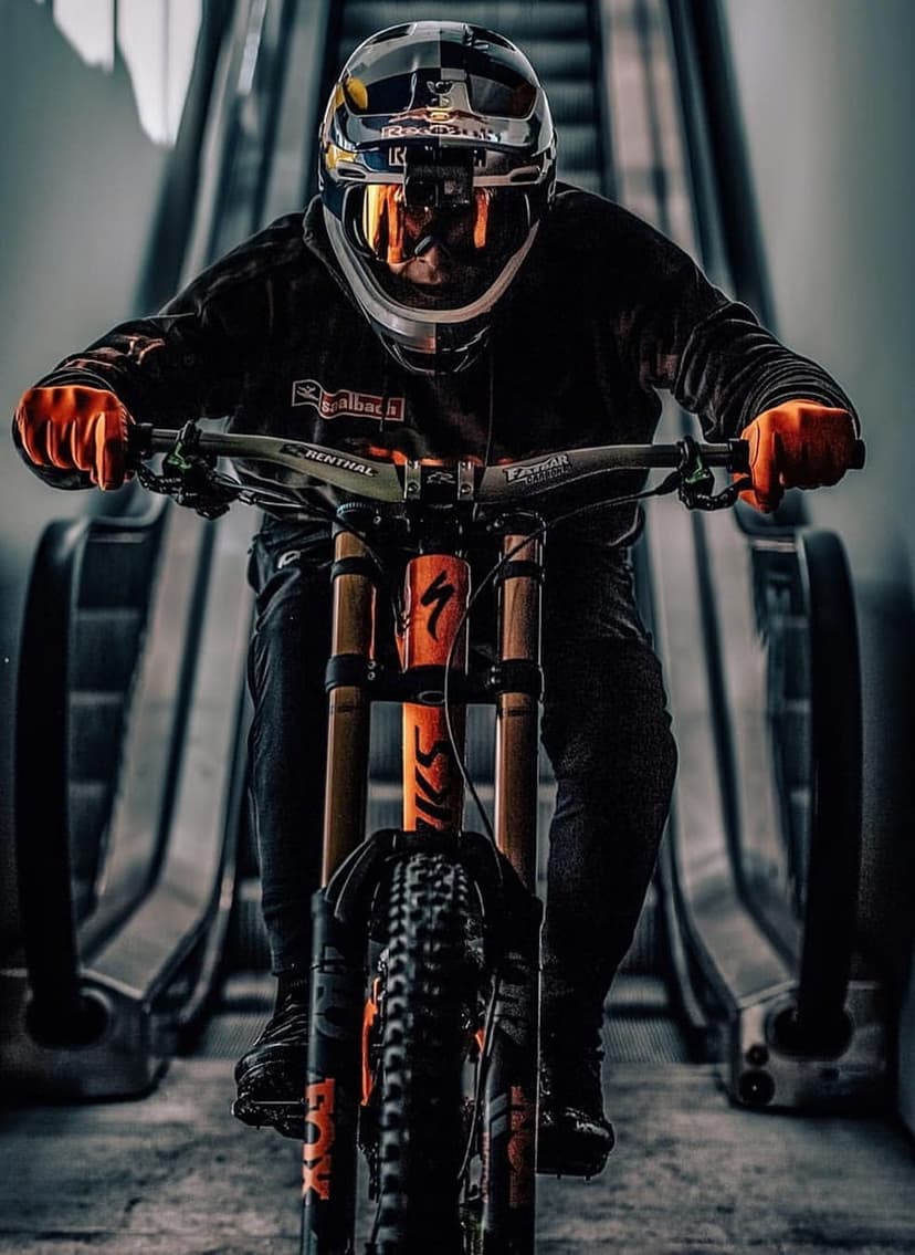 Mountain biker in orange gloves rides a specialized bicycle down a steep escalator with dramatic industrial lighting.