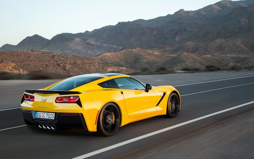 Yellow sports car driving on a desert highway with rugged mountains and golden hour lighting in the background.