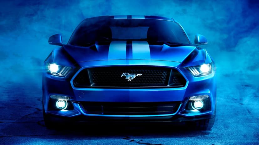 Blue Ford Mustang front view with glowing headlights and white racing stripes surrounded by thick blue smoke.