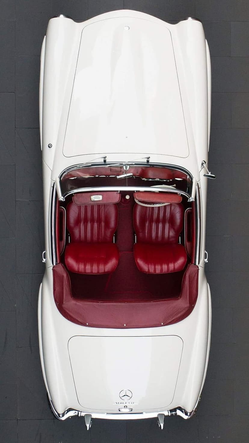 White Mercedes convertible viewed from above featuring red leather seats and chrome trim on a dark surface.