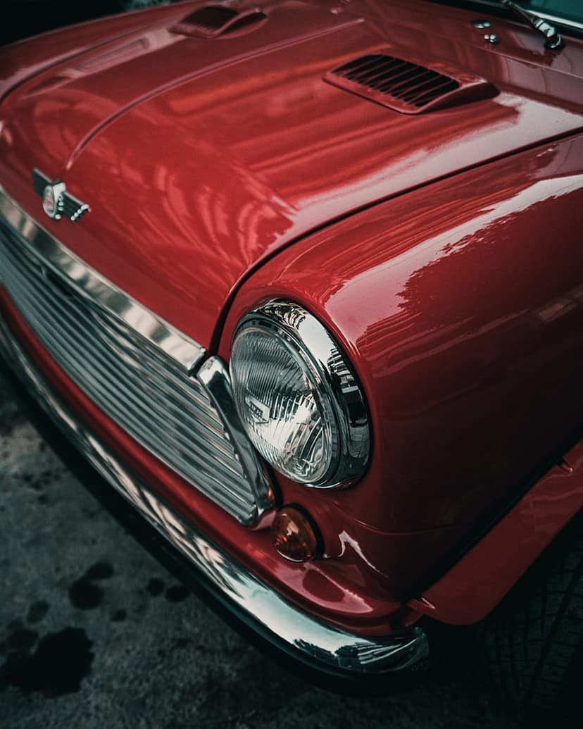 Red Mini Cooper front end featuring a round chrome headlight, slatted grille, and glossy scarlet paintwork.
