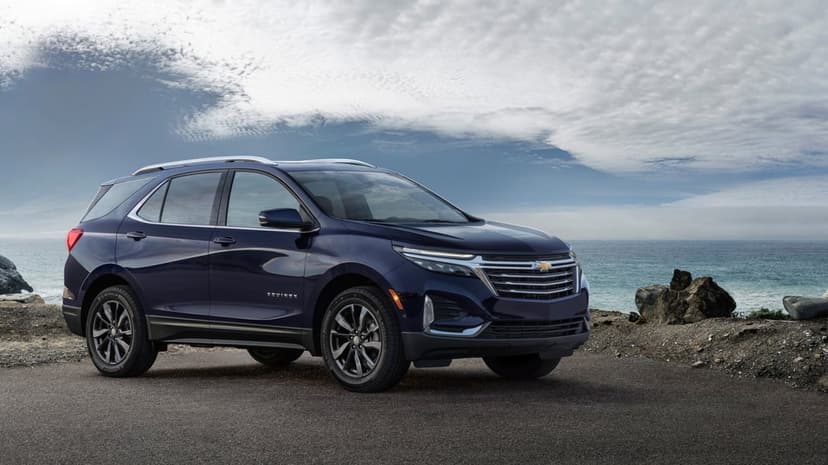 Dark blue Chevrolet Equinox SUV parked on a coastal road overlooking the ocean under a textured cloudy sky.